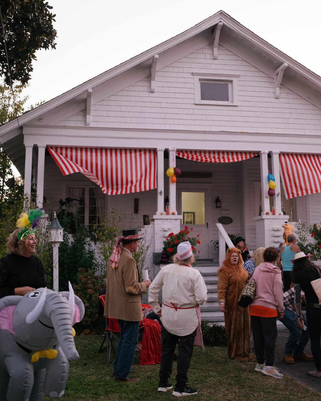 Beaufort NC Halloween neighborhood gathering with costumes and striped circus decorations on a white craftsman porch — captured by Beaufort NC photographer Hailey Rae Photography.