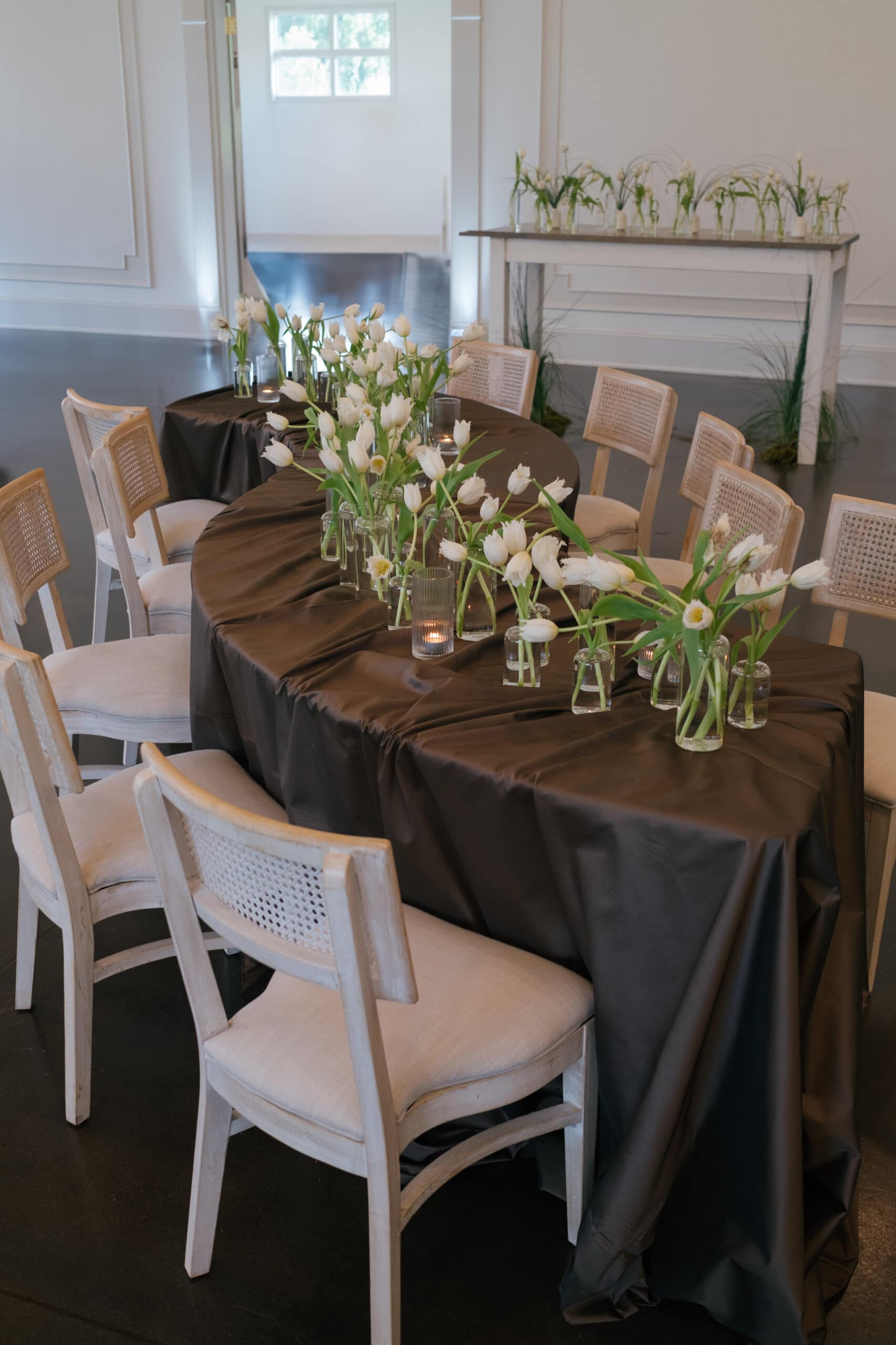 A clean table scape design with a curving reception table lined with hand tied floral arrangements